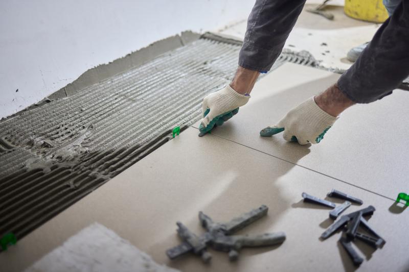 Ouvrier en combinaison grise et casque orange installant des plaques de placo sur un plafond intérieur